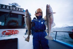 Bilde av en fisker som har fisket to fisk på en fiskebåt.