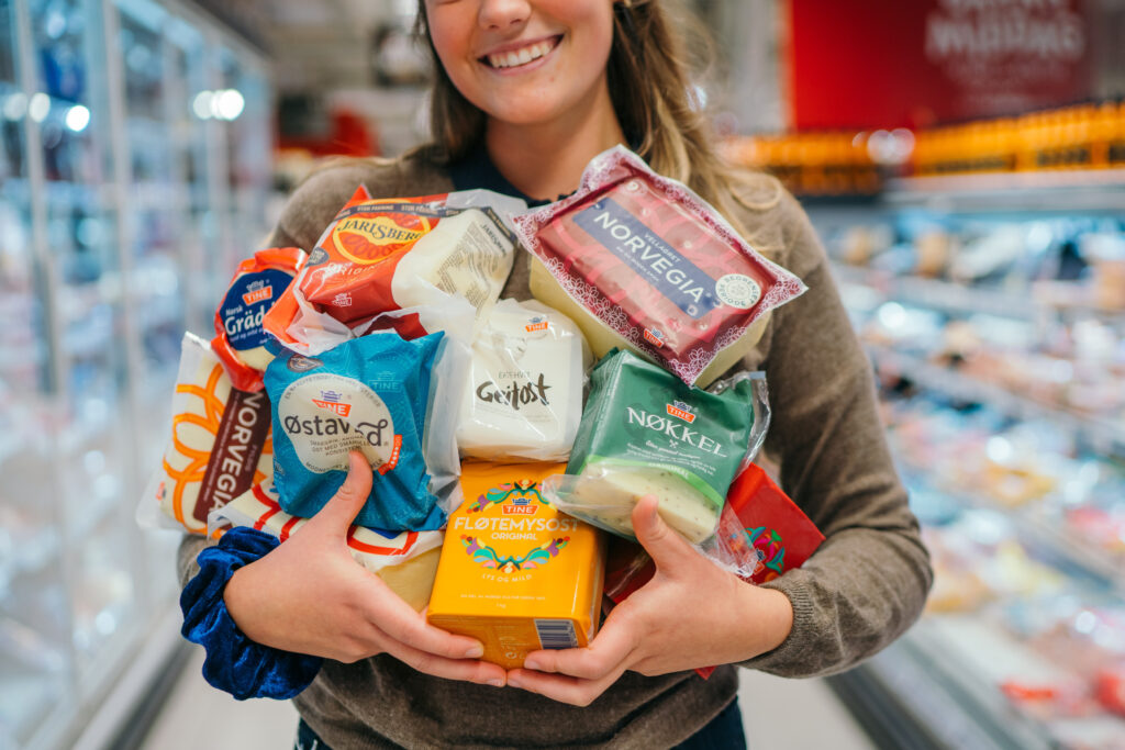 En dame med brunt hår holder flere Tine produkter i hendene inne i en matbutikk