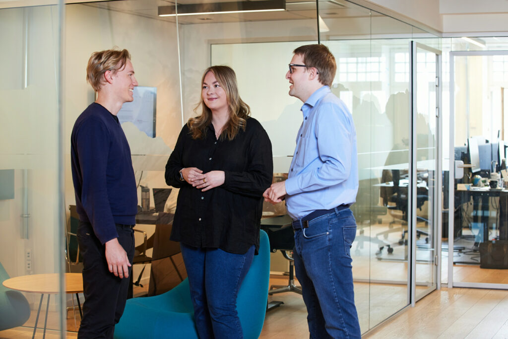 Tre personer i Promon som snakker sammen i kontorlandskapet