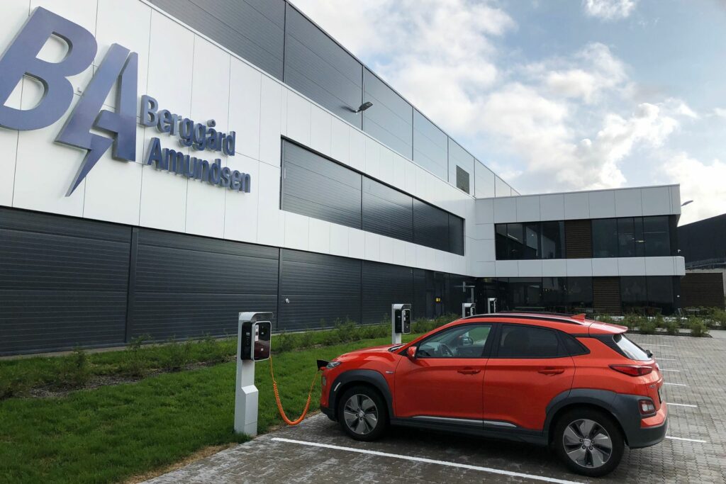 Utiden av Berggård Amundsens lokaler på Langhus, med en rød elbil som lader på fremsiden