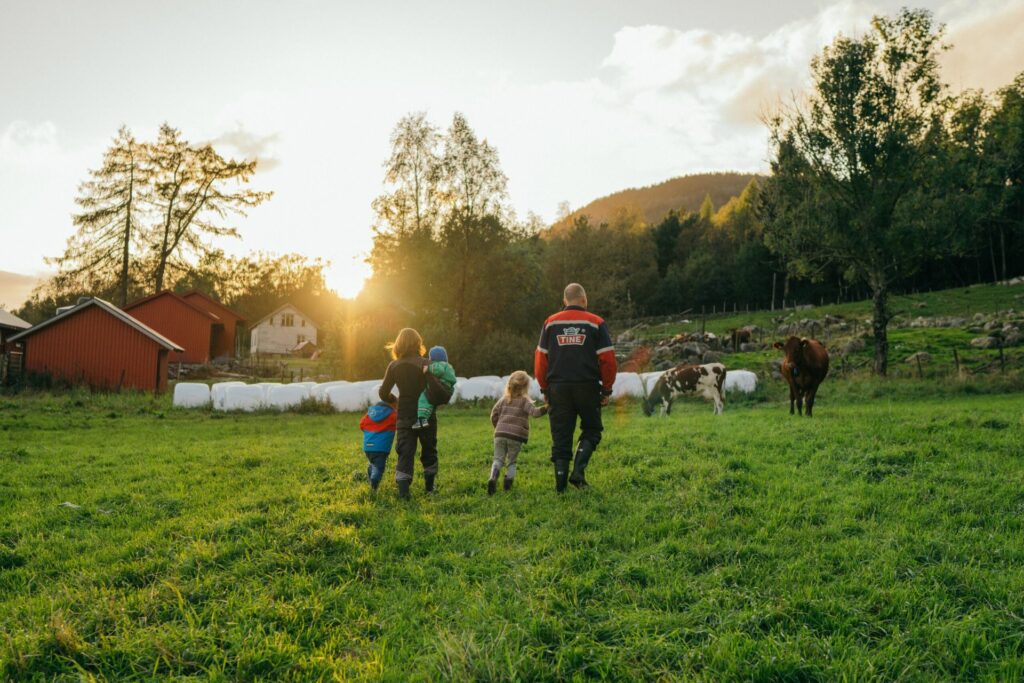 Bonde, kone og to barn er ute på et jorde med kuer, fjør og rundballer i bakgrunnen.