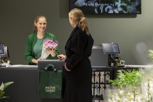 En kvinnelig kunde handler blomster av en smilende kassadame hos Mester Grønn