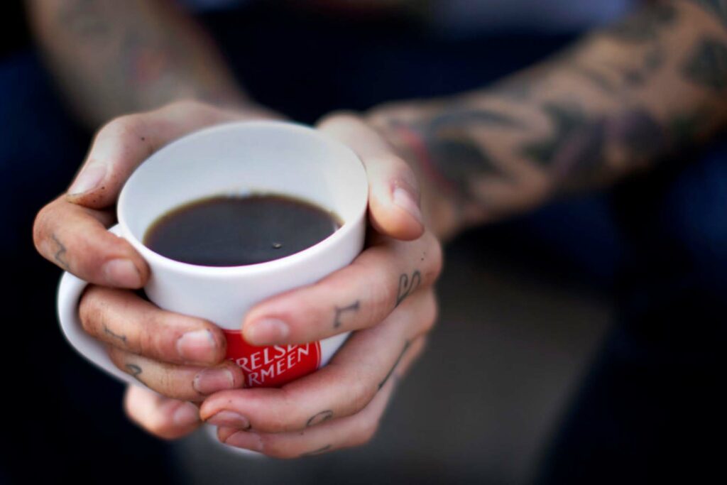 Tattooerte hender som holder rundt en Frelsesarmeen kopp med kaffe.