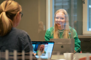Lyshåret dame i grønn genser sitter inne på et møterom sammen med en annen kvinnelig kollega