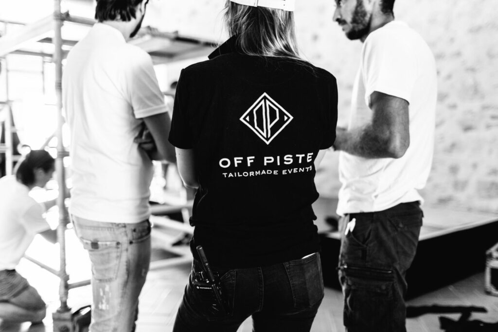 Kvinnelig ansatt med Off Piste logo på rygg snakker med to menn i hvite t-skjorter
