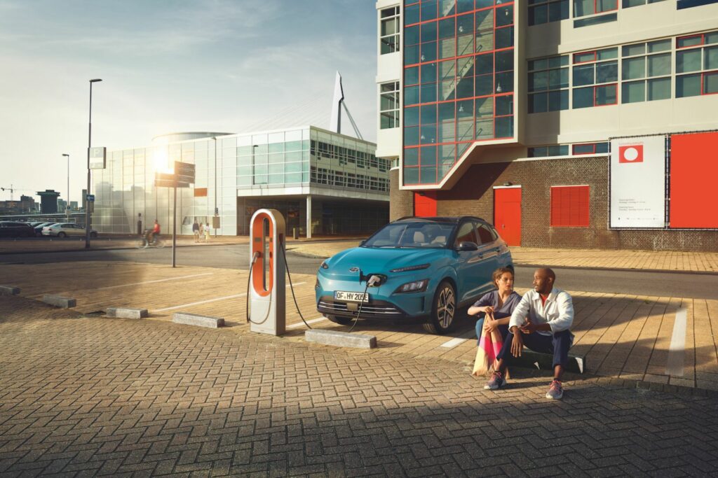 Mann og kvinne sitter ved siden av en Hyundai som lader